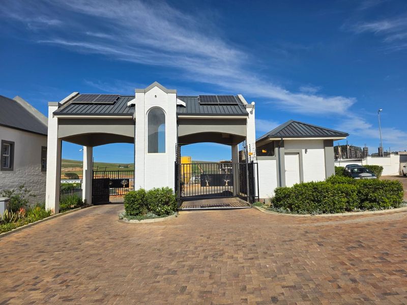 A well-maintained gated entrance to the townhouse complex featuring a security guard house, paved driveway, and solar-equipped roof structure.
