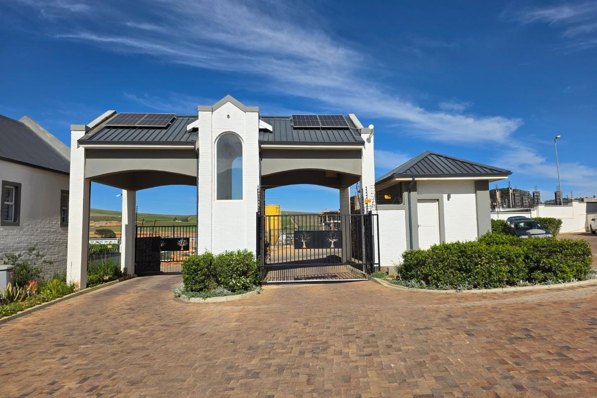 A well-maintained gated entrance to the townhouse complex featuring a security guard house, paved driveway, and solar-equipped roof structure.