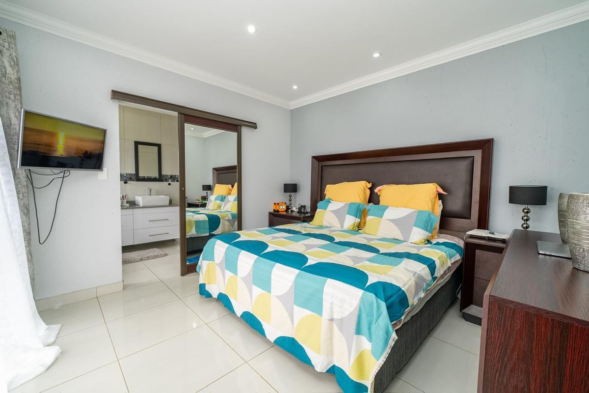A well-maintained bedroom featuring tiled flooring, recessed ceiling lighting, and an en-suite bathroom accessed via a sliding mirror door.