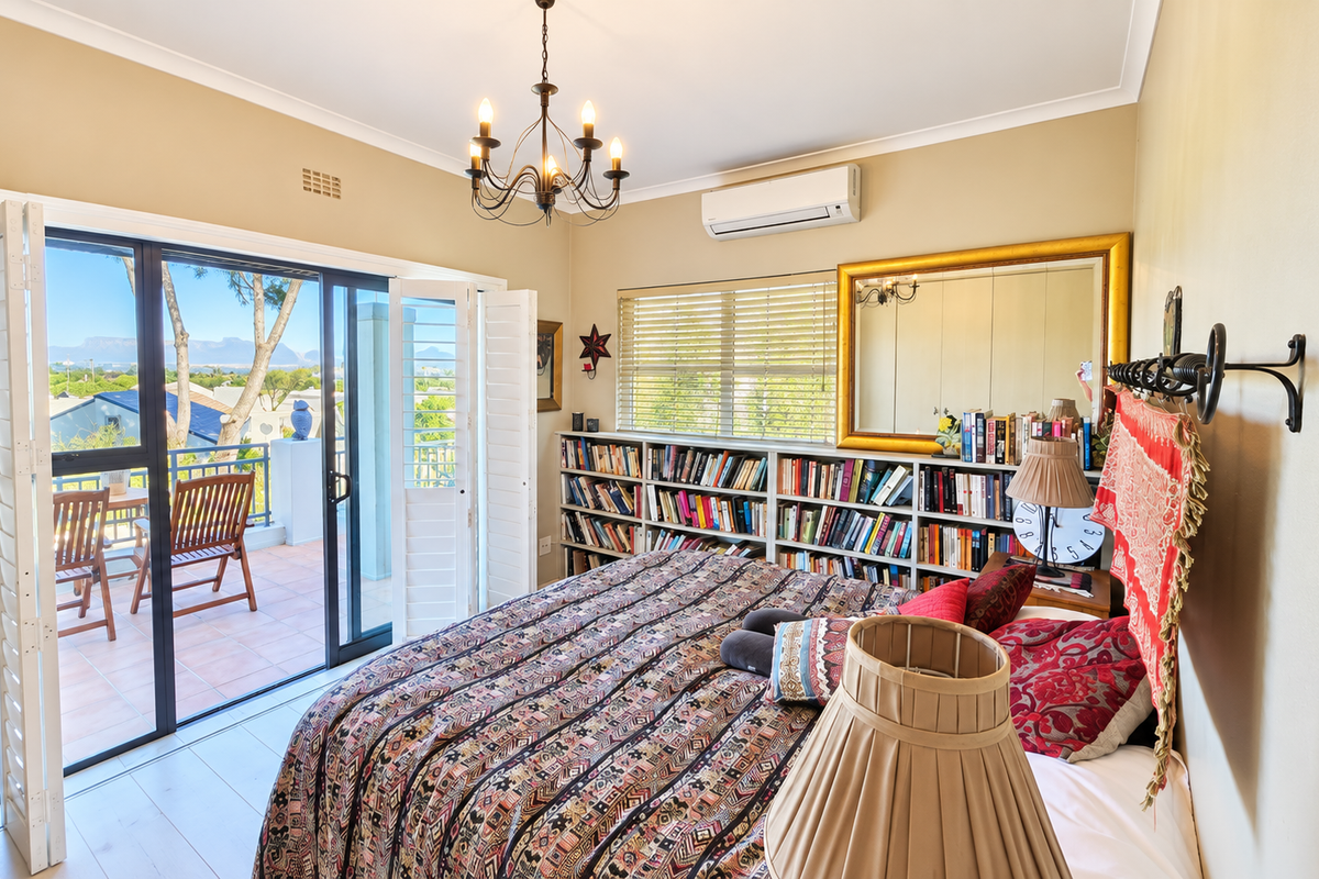 A well-maintained bedroom featuring built-in shelving, a split-system air conditioner, and sliding glass doors that open onto a private balcony with scenic views.