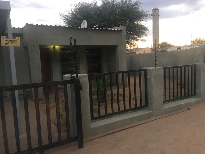 Front exterior view of a townhouse featuring a masonry boundary wall, metal security gate, and electric fencing.