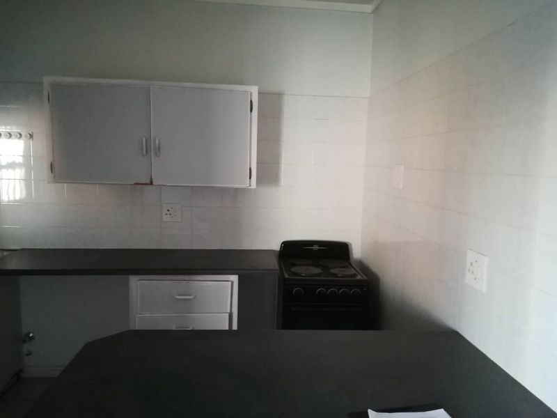 A functional kitchen space featuring built-in cabinetry, laminate countertops, and a freestanding electric stove with tiled splashback walls.