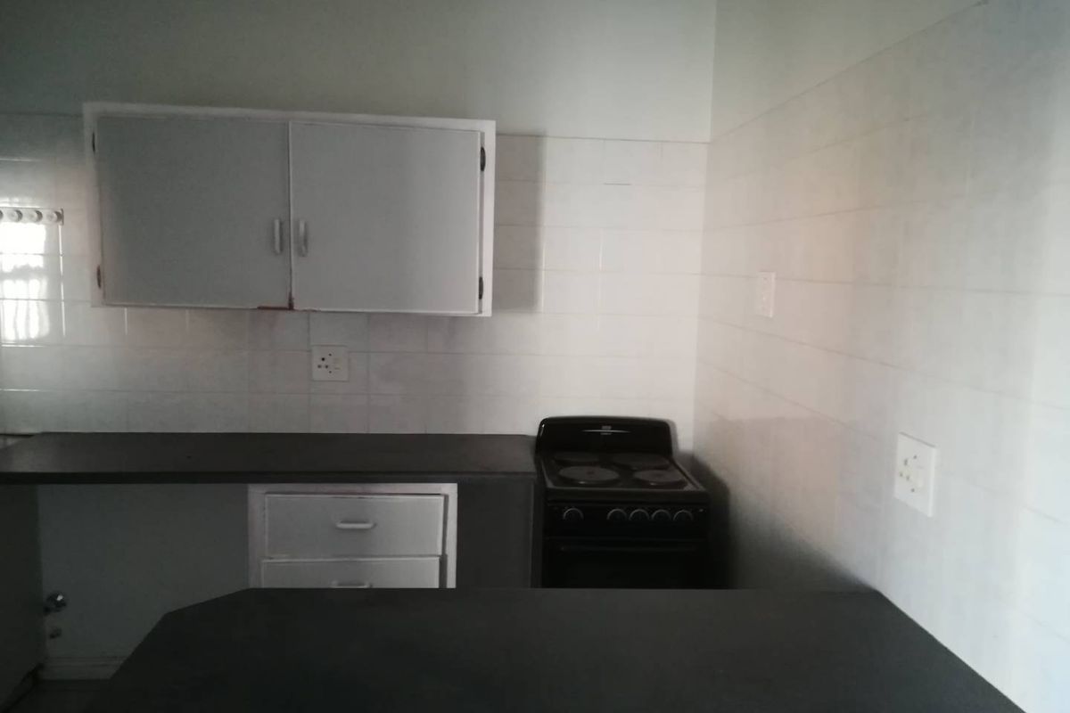 A functional kitchen space featuring built-in cabinetry, laminate countertops, and a freestanding electric stove with tiled splashback walls.