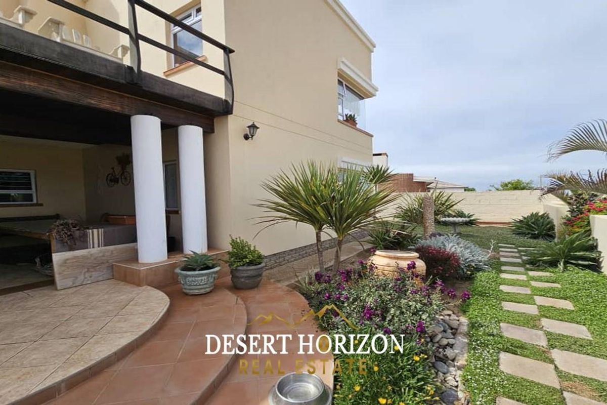 Rear view of the property featuring a covered patio area with columns, tiled flooring, and a landscaped garden with stone pathway.