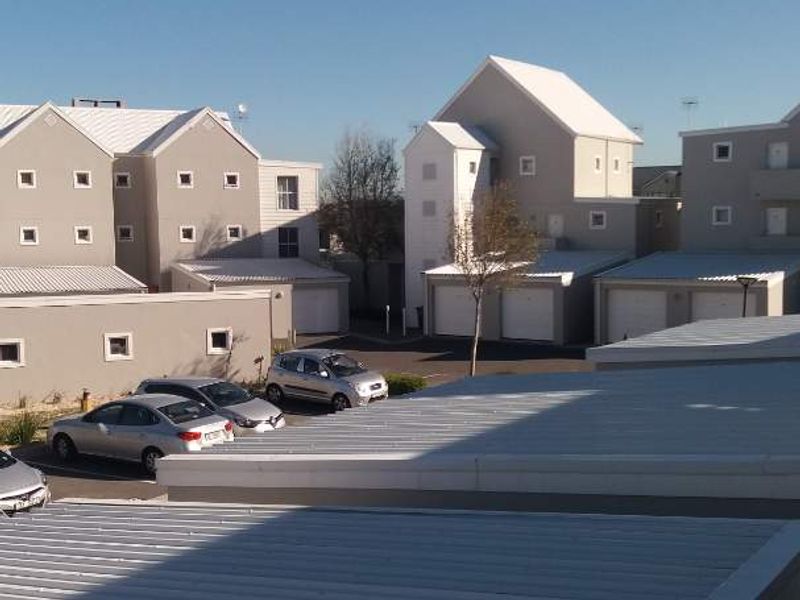 An elevated view of the apartment complex exterior, featuring corrugated metal roofing, garage units, and a paved driveway area.