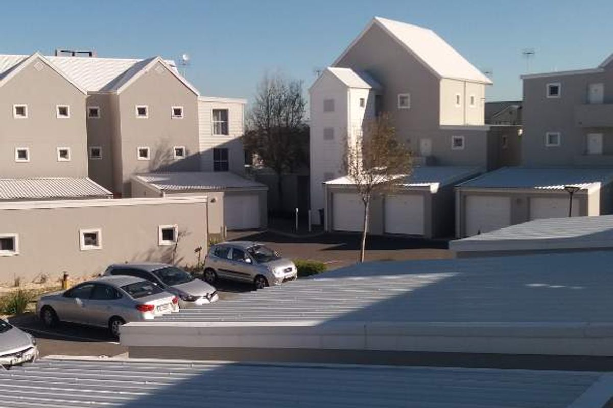 An elevated view of the apartment complex exterior, featuring corrugated metal roofing, garage units, and a paved driveway area.