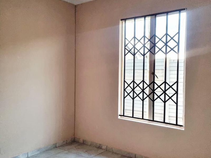 A clean, empty bedroom featuring neutral wall tones, tiled flooring, and a window fitted with a security gate.
