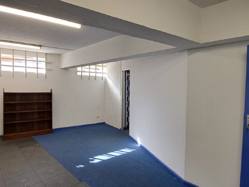 A functional utility space featuring exposed ceiling beams, security-barred windows, and durable flooring, suitable for storage or workshop use.