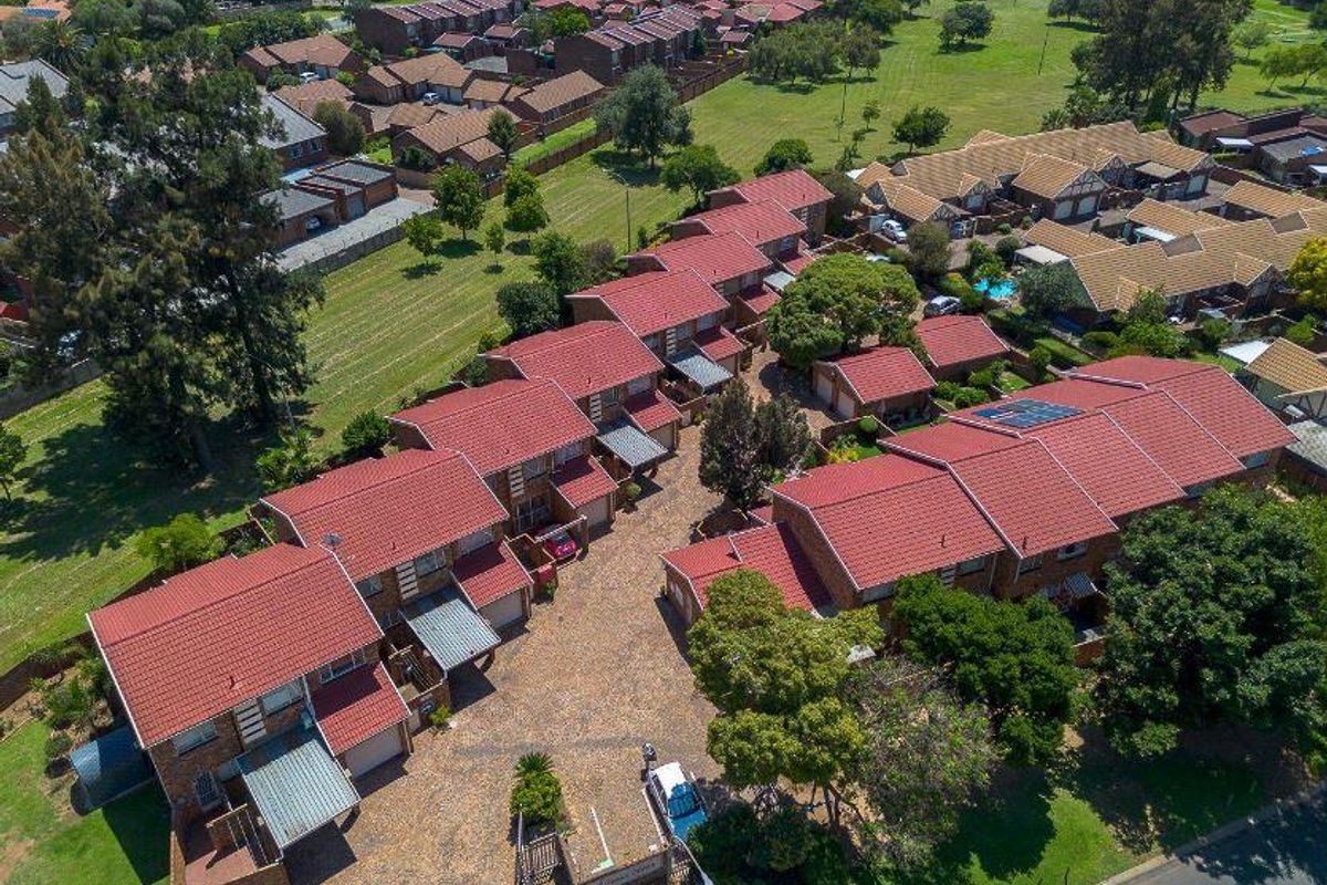 Aerial view of a townhouse complex featuring red tiled roofs, paved driveways, and surrounding green communal garden spaces.