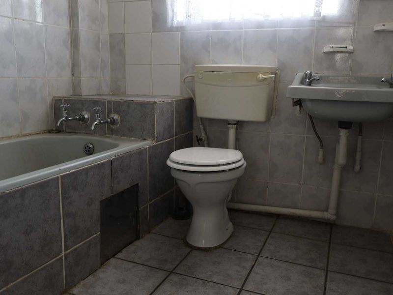 A dated bathroom featuring a bathtub, toilet, and wall-mounted basin with original ceramic tiling throughout, offering significant potential for a modern renovation.