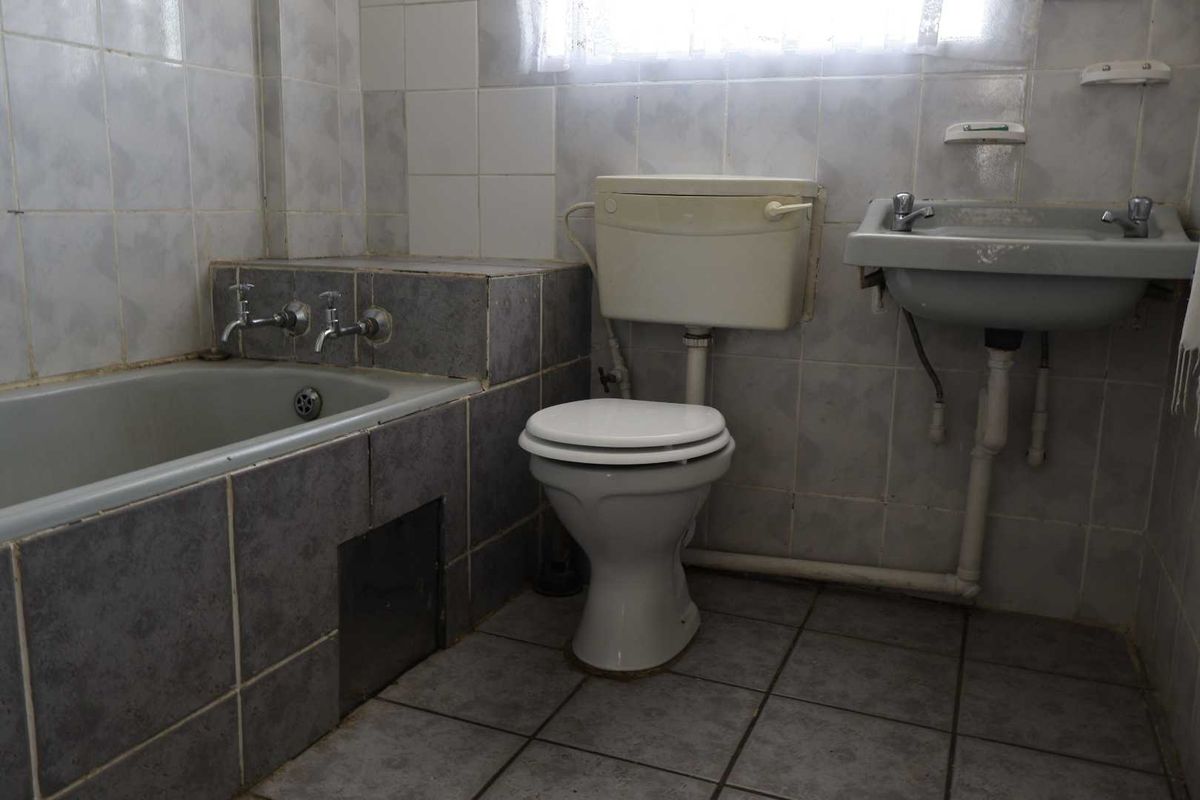 A dated bathroom featuring a bathtub, toilet, and wall-mounted basin with original ceramic tiling throughout, offering significant potential for a modern renovation.