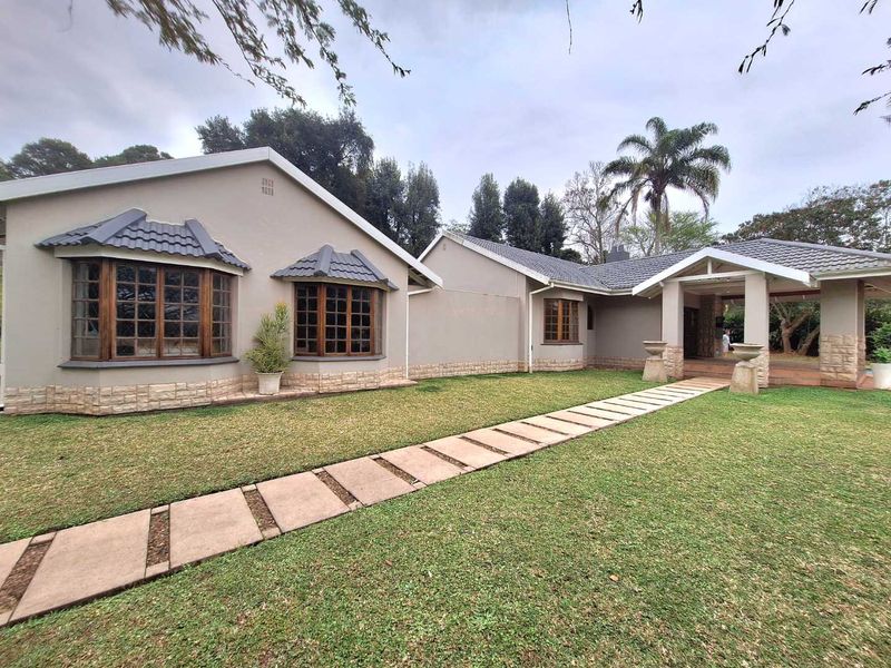 Front elevation of a well-maintained house featuring stone cladding, bay windows, timber frames, and a paved walkway leading to a covered entrance.