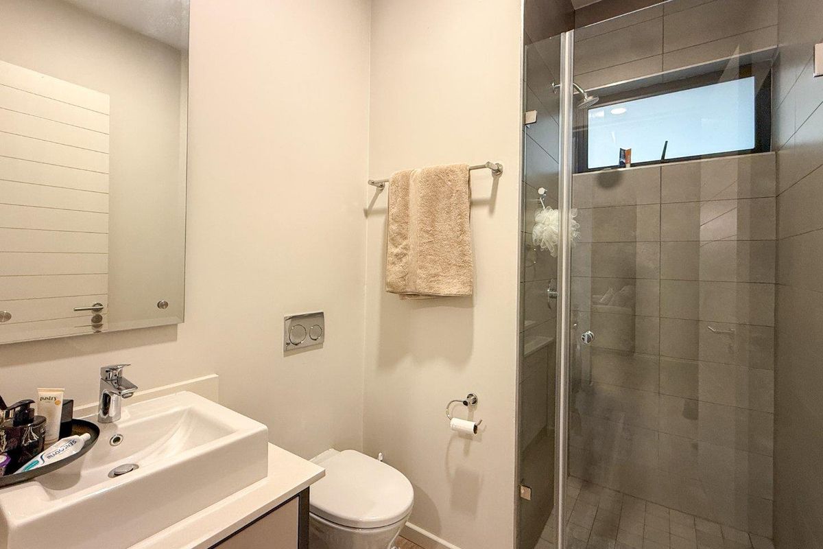A modern bathroom featuring a vanity with a ceramic basin, a wall-mounted mirror, a toilet, and a glass-enclosed shower with tiled walls.