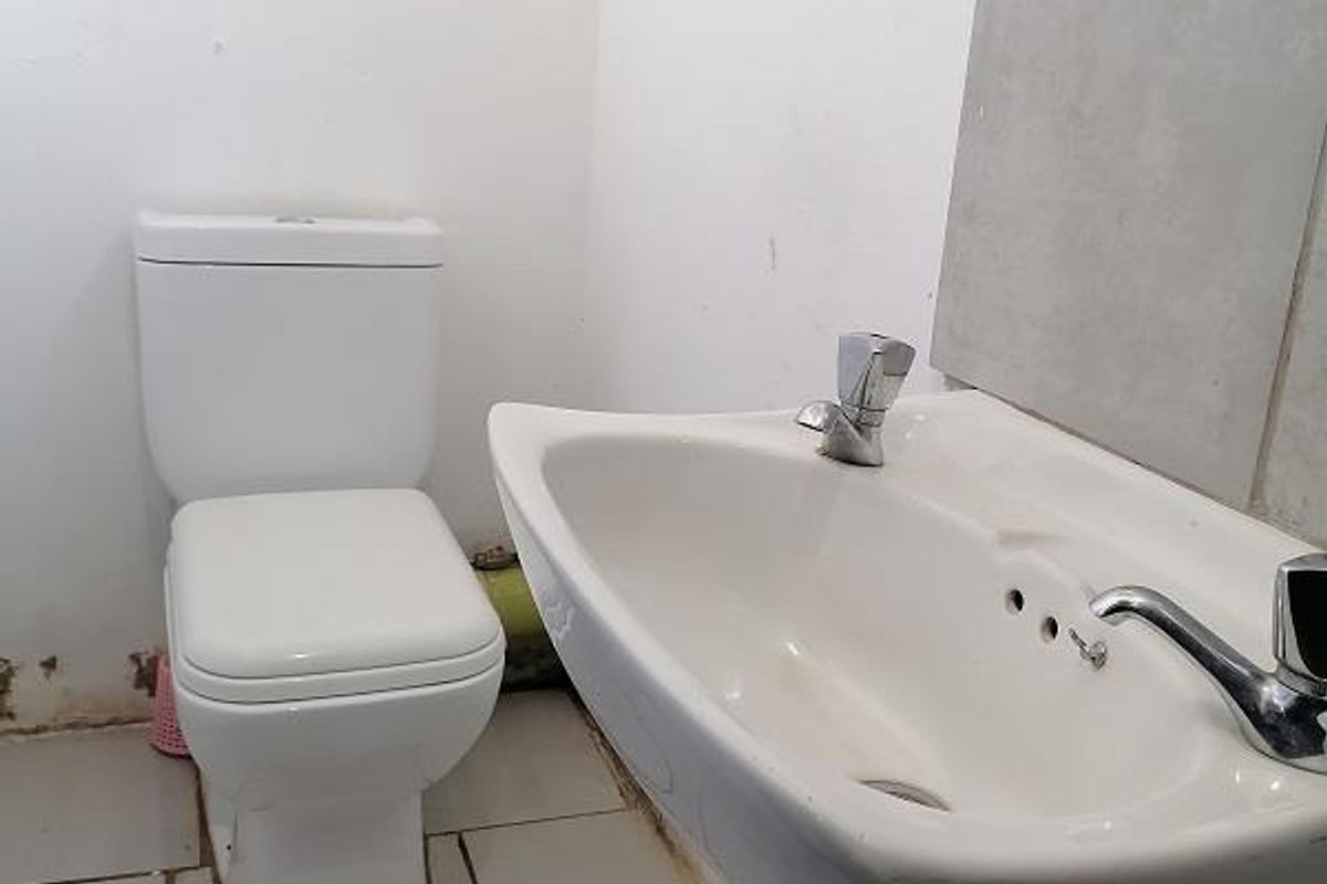A functional bathroom featuring a pedestal basin and toilet with tiled flooring and splashback, presenting a clean but dated aesthetic.