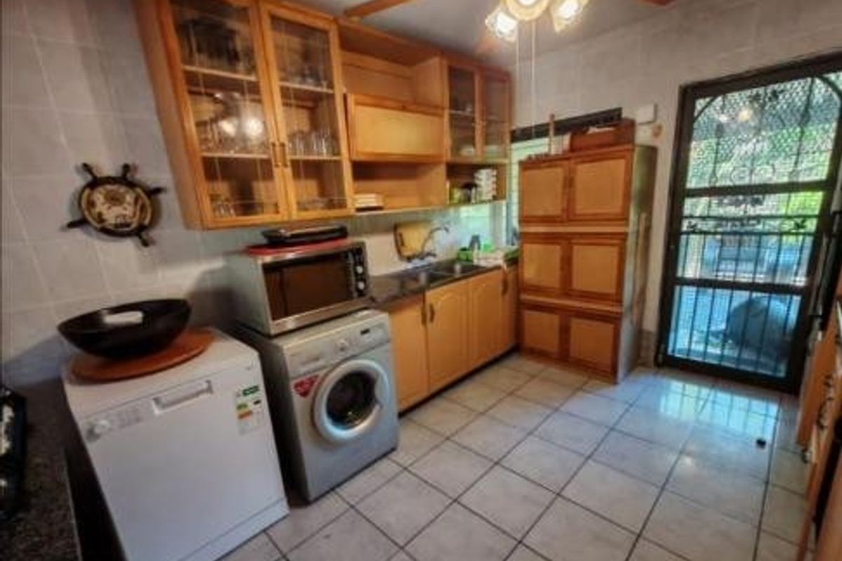 A functional kitchen featuring wooden cabinetry, tiled flooring, and a security gate leading to the exterior.