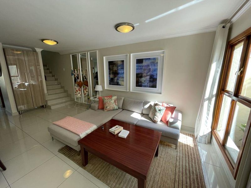 A bright living room featuring tiled flooring, a staircase, built-in cabinetry, and large wooden-framed windows allowing for natural light.