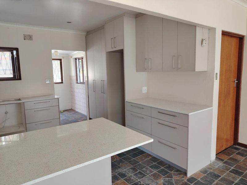 A clean, modern kitchen featuring neutral-toned built-in cabinetry, stone countertops, a central island, and durable tiled flooring.