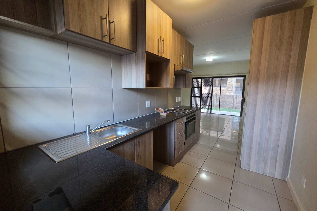 Modern open-plan kitchen featuring wood-finish cabinetry, granite countertops, and integrated appliances, flowing into a bright living area with access to an outdoor space.