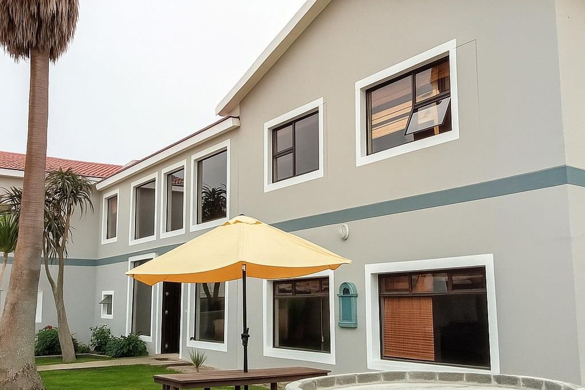 A view of the rear exterior of the guest house, featuring a landscaped garden area, paved pathways, and a brick-built circular feature.
