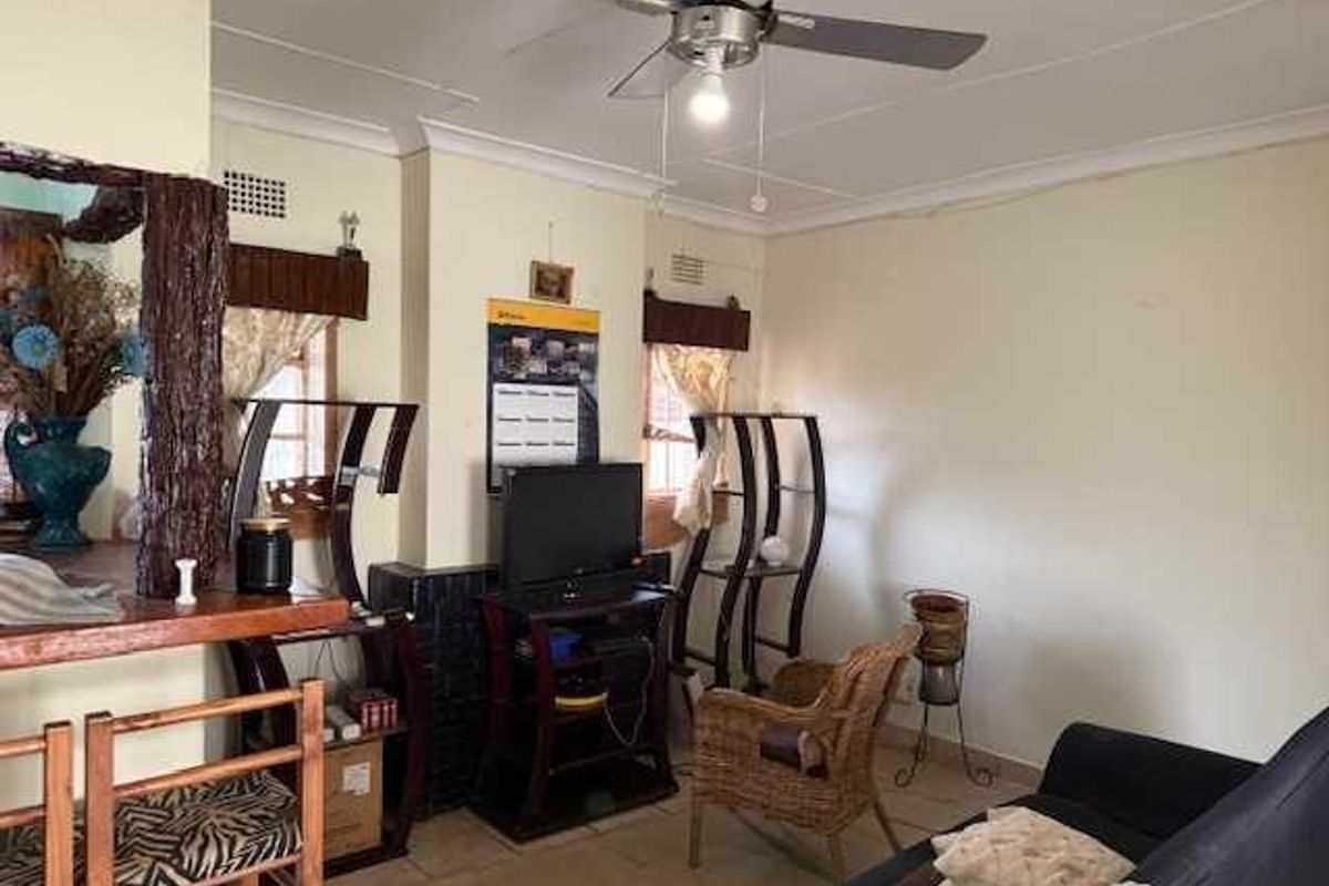 A living room area featuring a ceiling fan, tiled flooring, and a breakfast bar counter with a decorative wooden pillar.