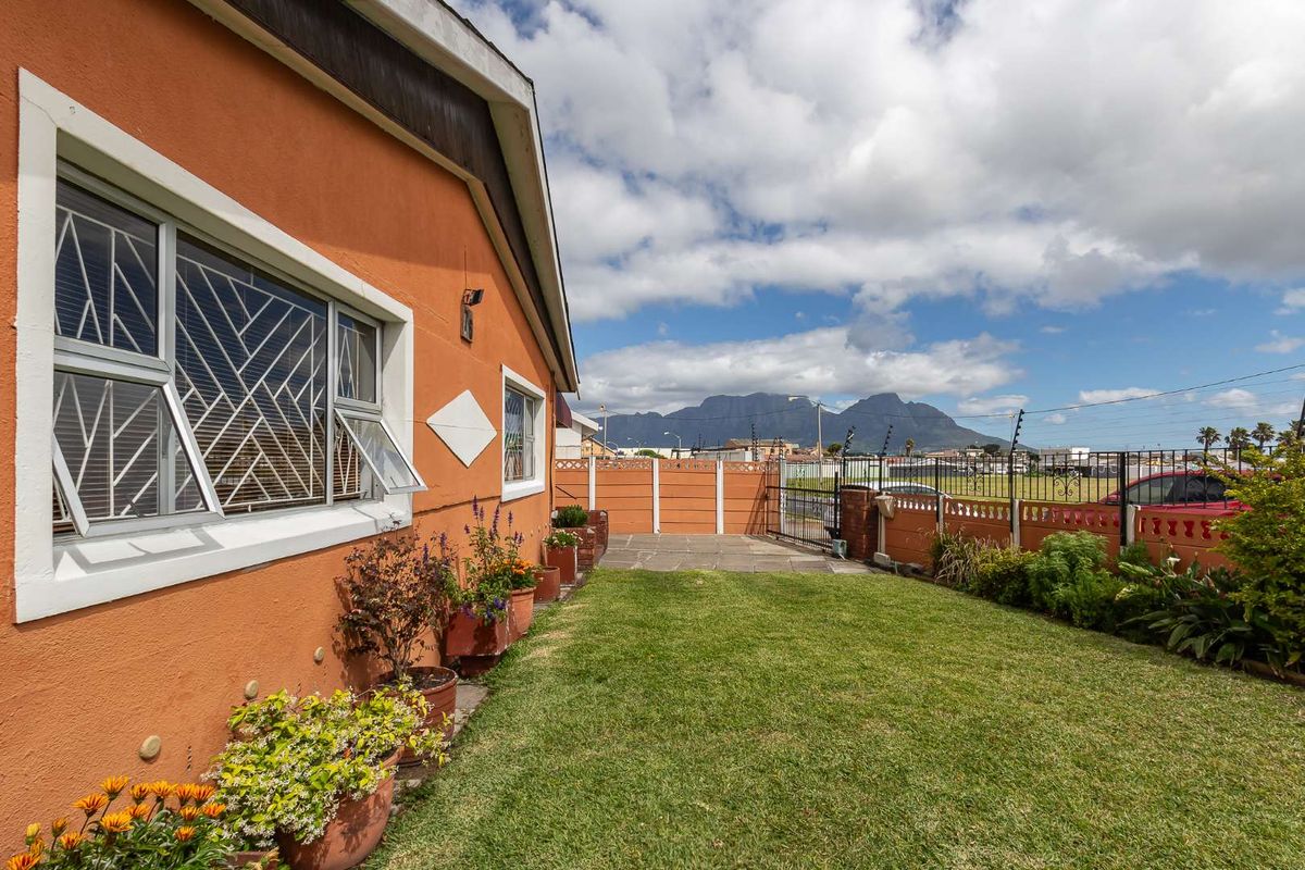 A rear garden area featuring a lawn, paved section, and perimeter wall with electric fencing, offering a view of the mountains.