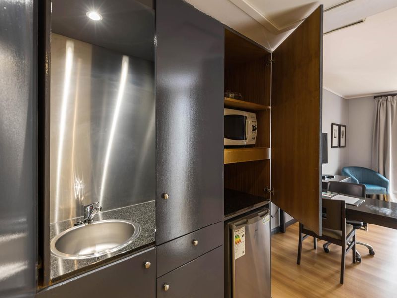 Compact kitchenette featuring dark cabinetry, granite countertops, a stainless steel sink, and integrated storage, seamlessly blending into the living area.