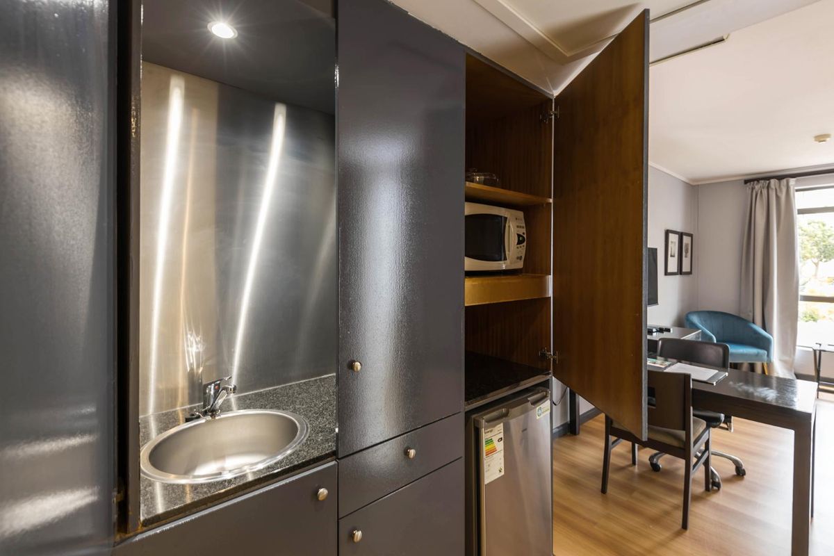 Compact kitchenette featuring dark cabinetry, granite countertops, a stainless steel sink, and integrated storage, seamlessly blending into the living area.