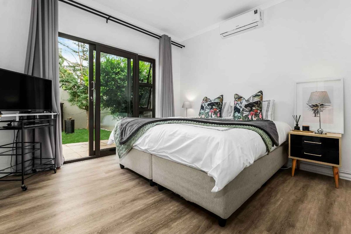 Bright bedroom featuring wood-look flooring, a wall-mounted air conditioning unit, and sliding glass doors providing direct access to the rear garden.