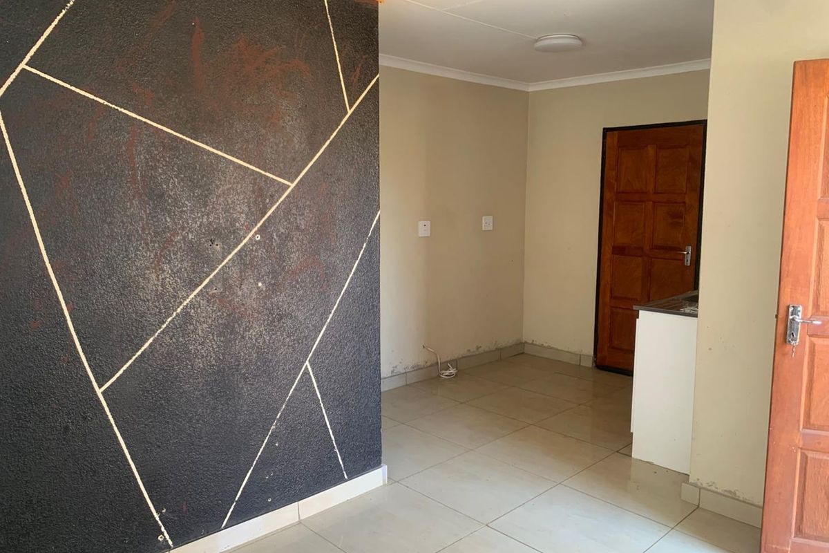 An empty interior space featuring tiled flooring, a decorative textured feature wall, and a wooden door leading to an adjacent area.