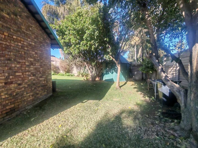 A view of the rear garden featuring a brick exterior wall, established trees, a garden shed, and perimeter timber fencing.