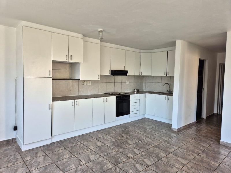 A functional kitchen featuring white built-in cabinetry, stone countertops, a tiled backsplash, and integrated cooking appliances with neutral tiled flooring.