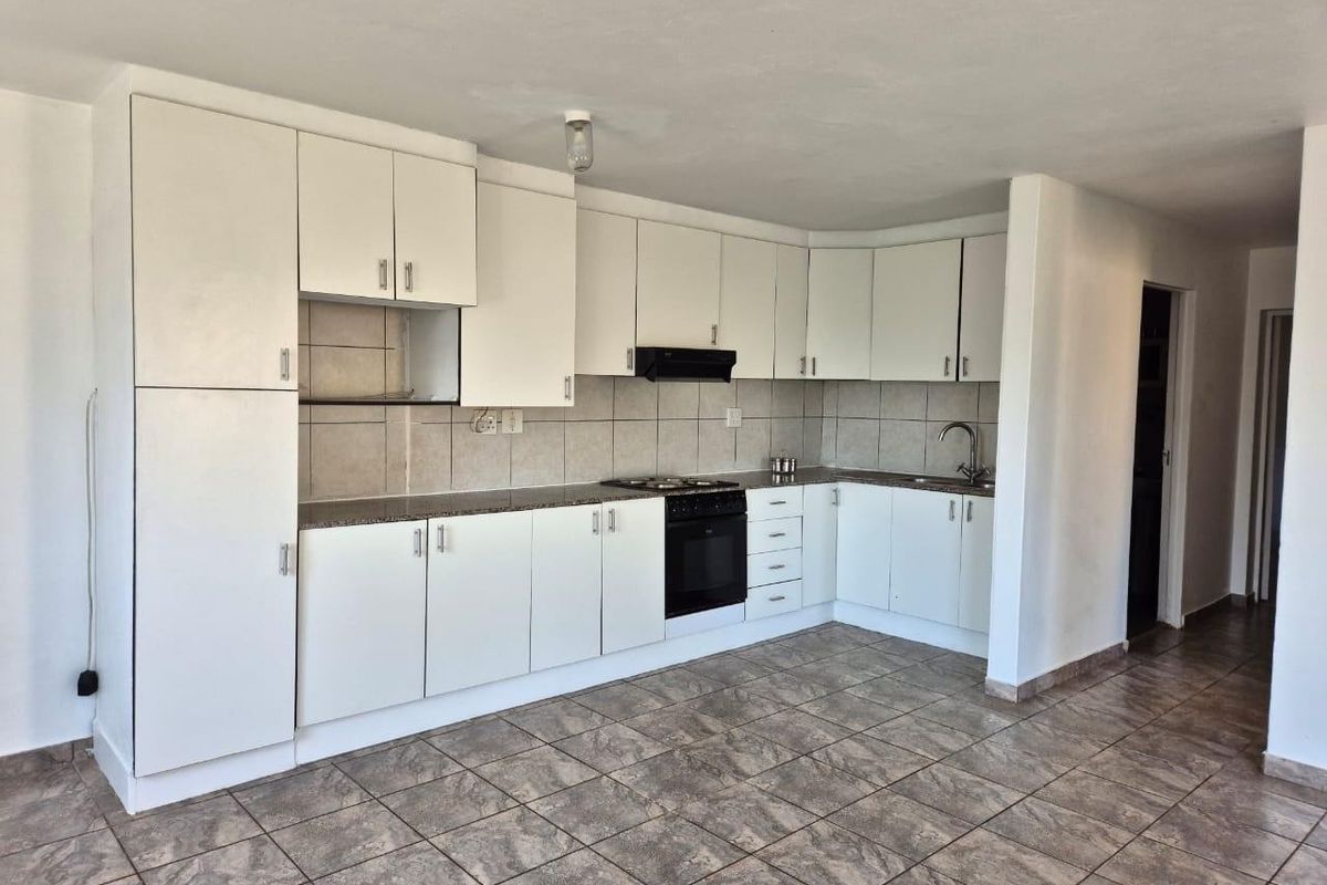A functional kitchen featuring white built-in cabinetry, stone countertops, a tiled backsplash, and integrated cooking appliances with neutral tiled flooring.