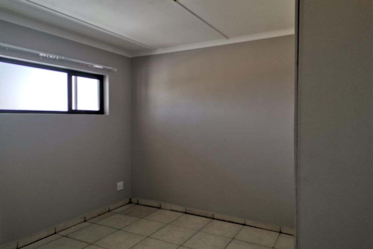 An empty bedroom featuring neutral wall paint, tiled flooring, and a window with a curtain rail.