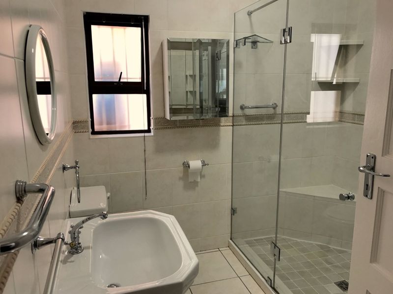A clean, well-maintained bathroom featuring a glass-enclosed shower with a built-in bench, pedestal sink, and neutral wall tiling.