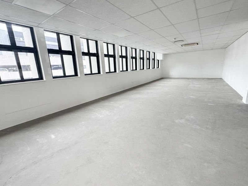 A spacious, vacant office area featuring a suspended ceiling, recessed lighting, ducted air conditioning, and a long row of large windows providing ample natural light.