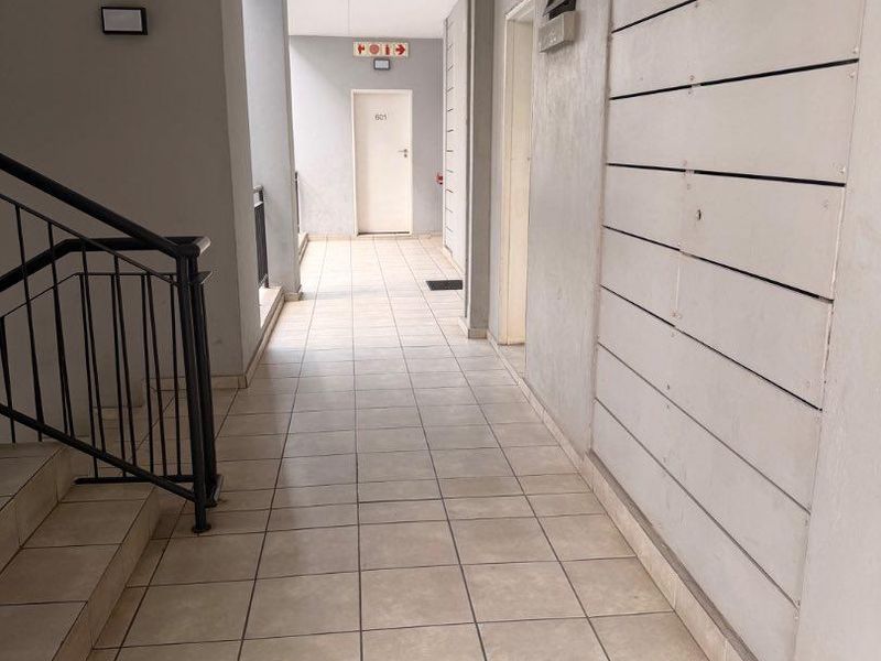 A functional apartment building hallway featuring tiled flooring, a metal staircase handrail, and standard emergency exit signage.