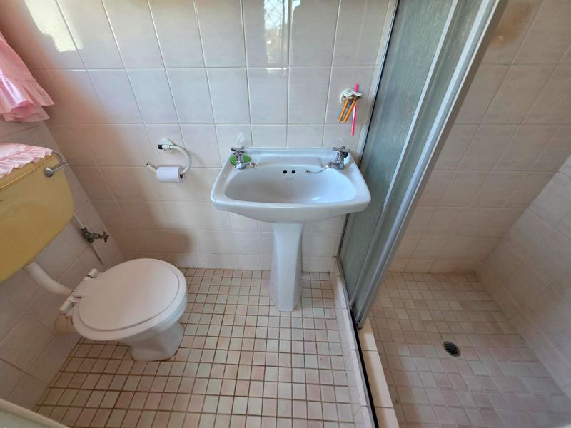 A compact bathroom featuring a pedestal basin, shower enclosure, and toilet, finished with dated ceramic wall and floor tiles.