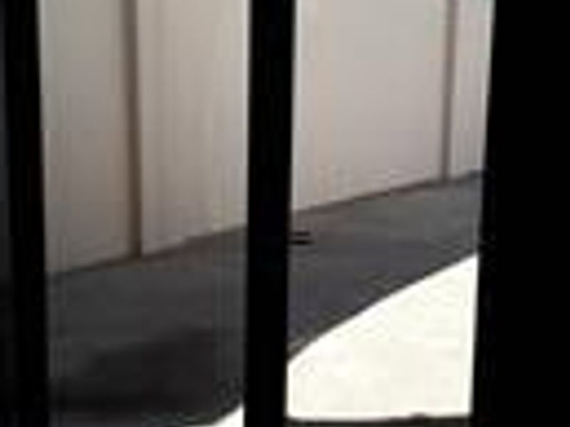 A view through a sliding glass door looking out onto a paved rear courtyard enclosed by a high boundary wall.