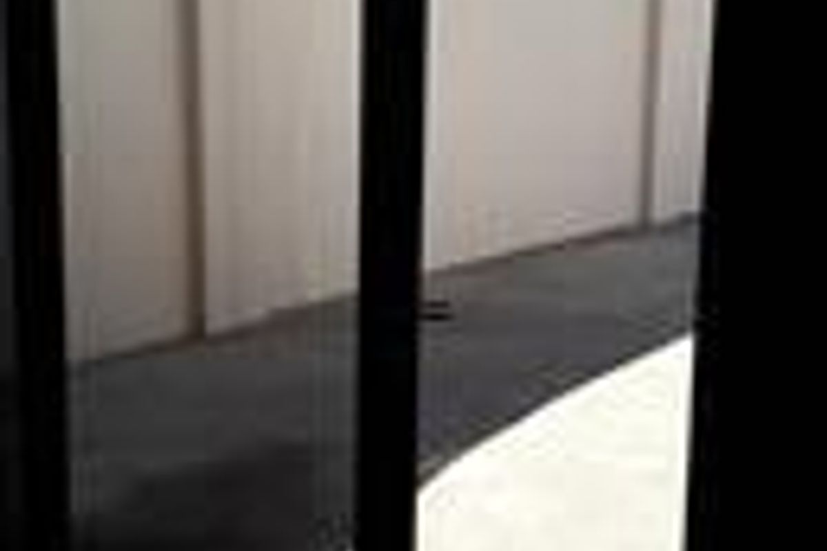A view through a sliding glass door looking out onto a paved rear courtyard enclosed by a high boundary wall.
