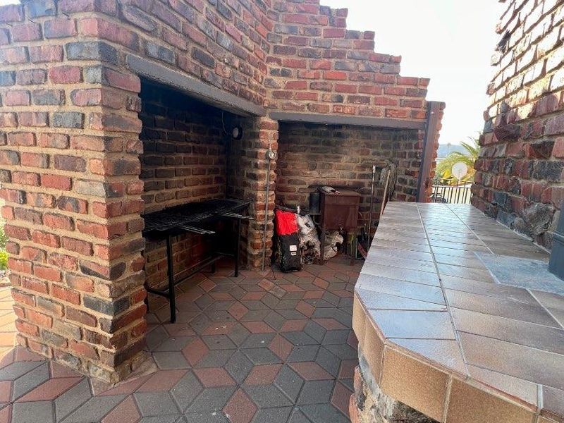 Outdoor patio area featuring a large built-in brick braai with chimney and a tiled preparation counter, perfect for outdoor entertaining.