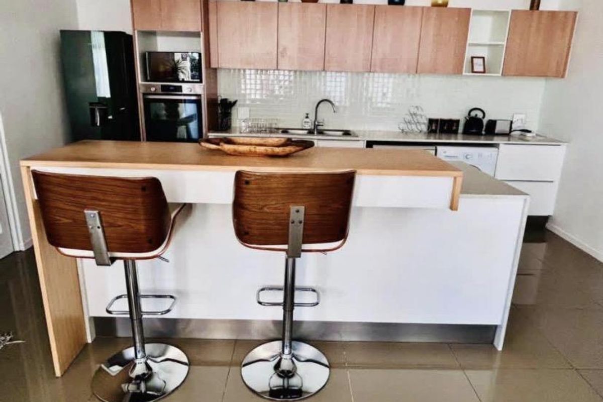 Modern kitchen featuring light wood-tone upper cabinetry, white base units, a breakfast bar, and integrated appliances including an oven and microwave.