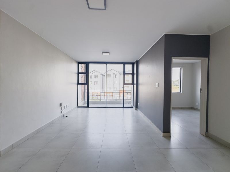 A bright, open-plan living area featuring neutral tiled flooring, modern grey accent walls, and large sliding glass doors leading to a balcony.