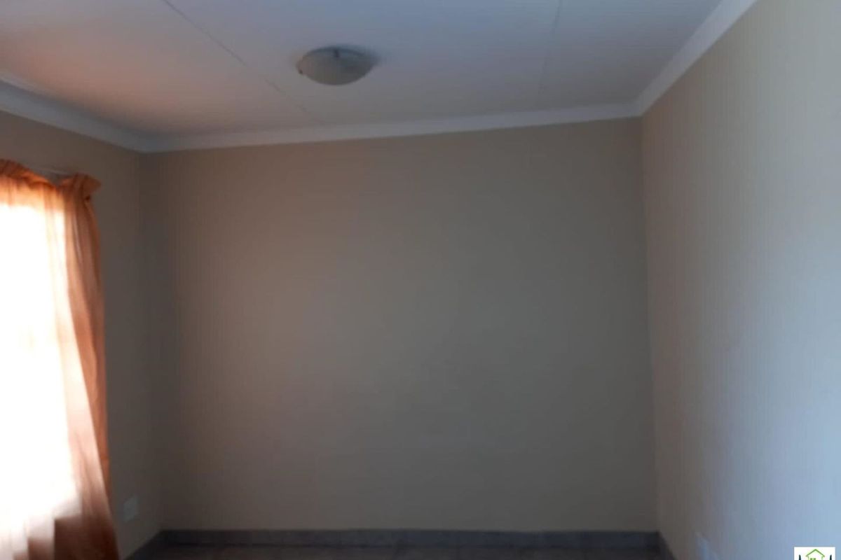 A simple, empty bedroom featuring neutral wall paint, tiled flooring, and a ceiling-mounted light fixture.