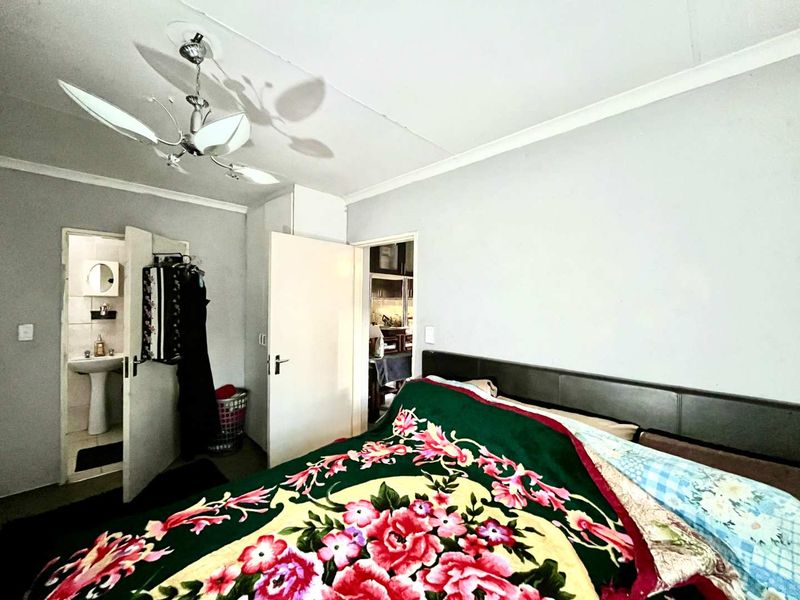 A bedroom featuring a coved ceiling and an attached en-suite bathroom with a pedestal basin, showing signs of wear including ceiling cracks.