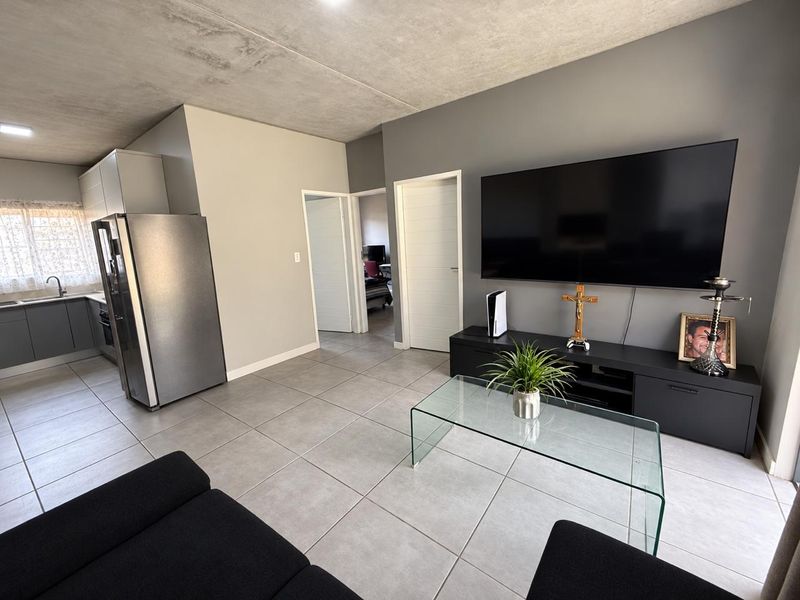Open-plan living area featuring tiled floors and an exposed concrete ceiling, seamlessly connected to a modern kitchen with built-in cabinetry.