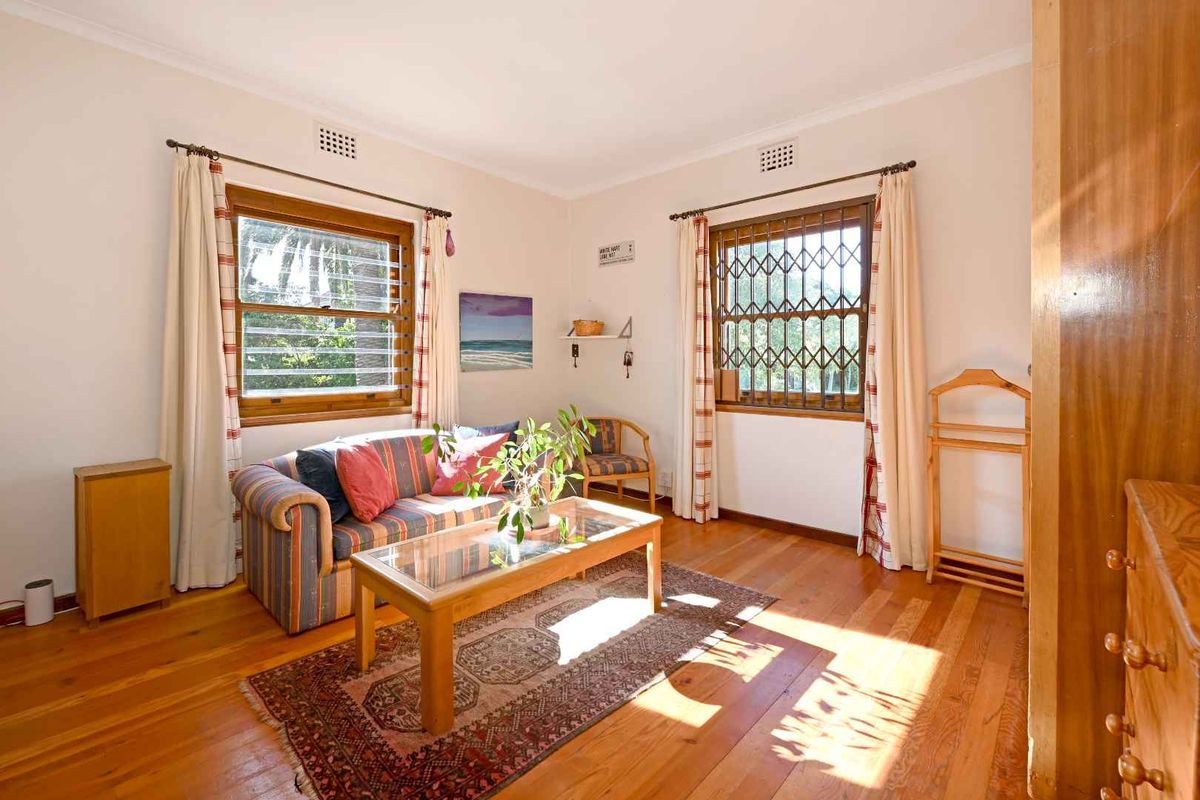 A living room featuring polished timber flooring, louver windows with security bars, and classic cornice detailing.