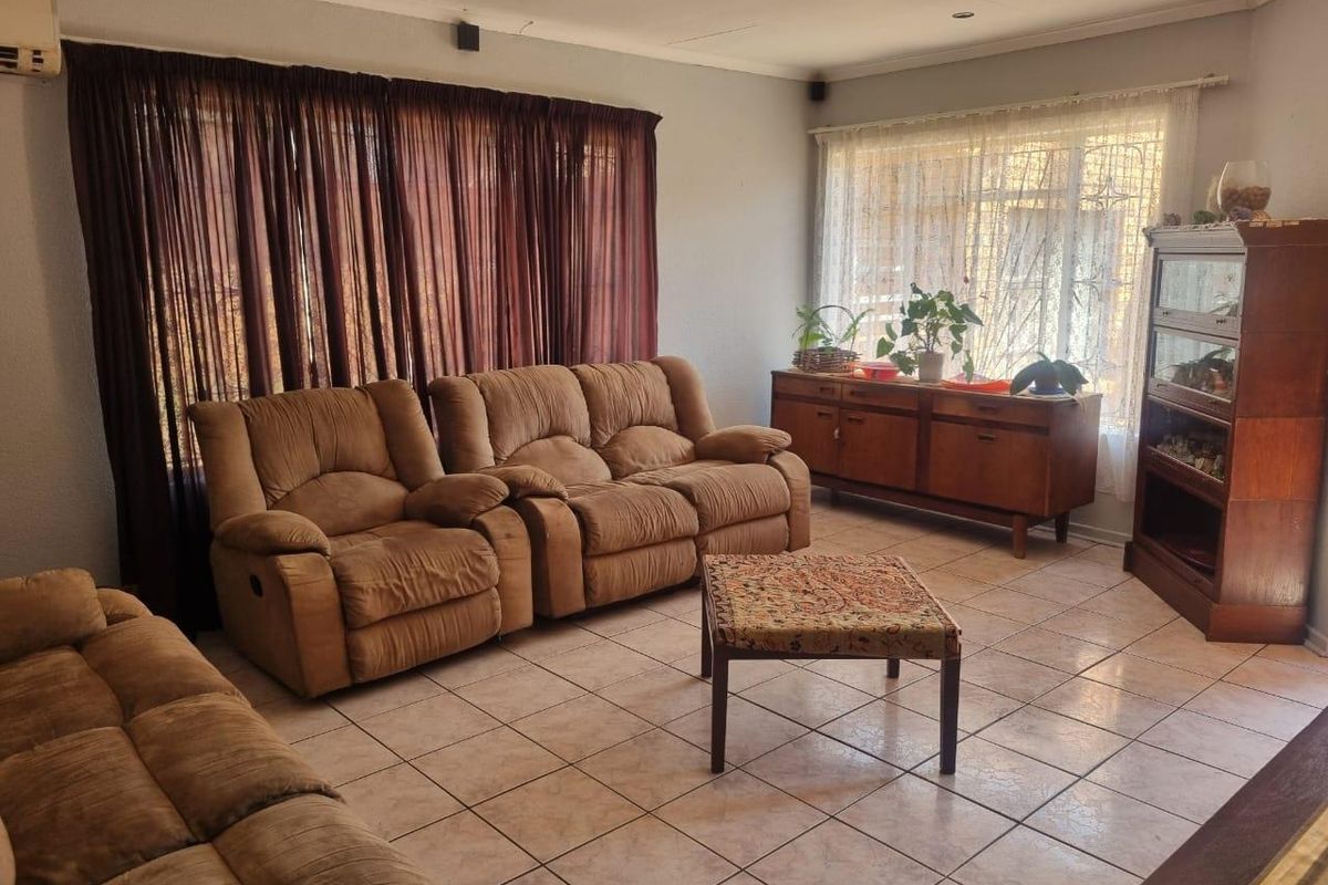 A spacious living room featuring ceramic tile flooring, large windows with security bars, and a wall-mounted air conditioning unit.