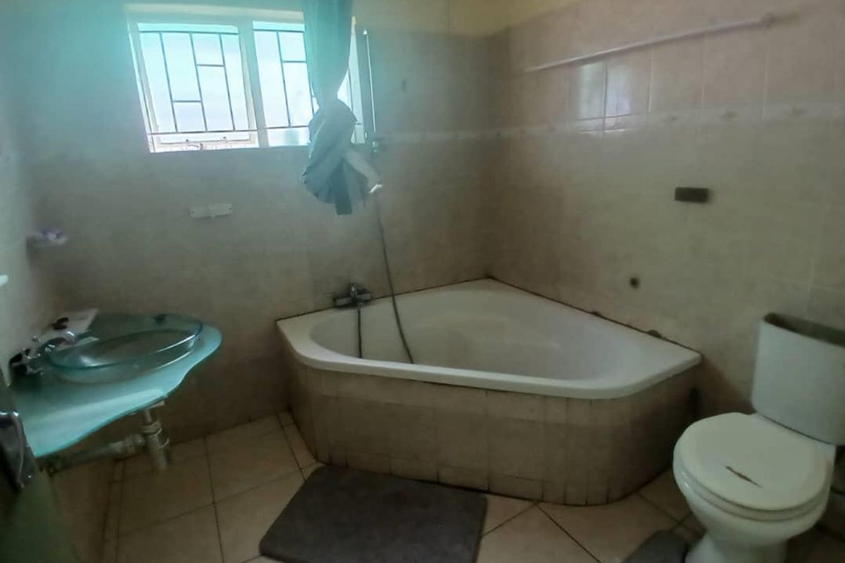 A dated bathroom featuring a corner bathtub, a glass vessel sink, and a standard toilet with tiled walls and flooring.