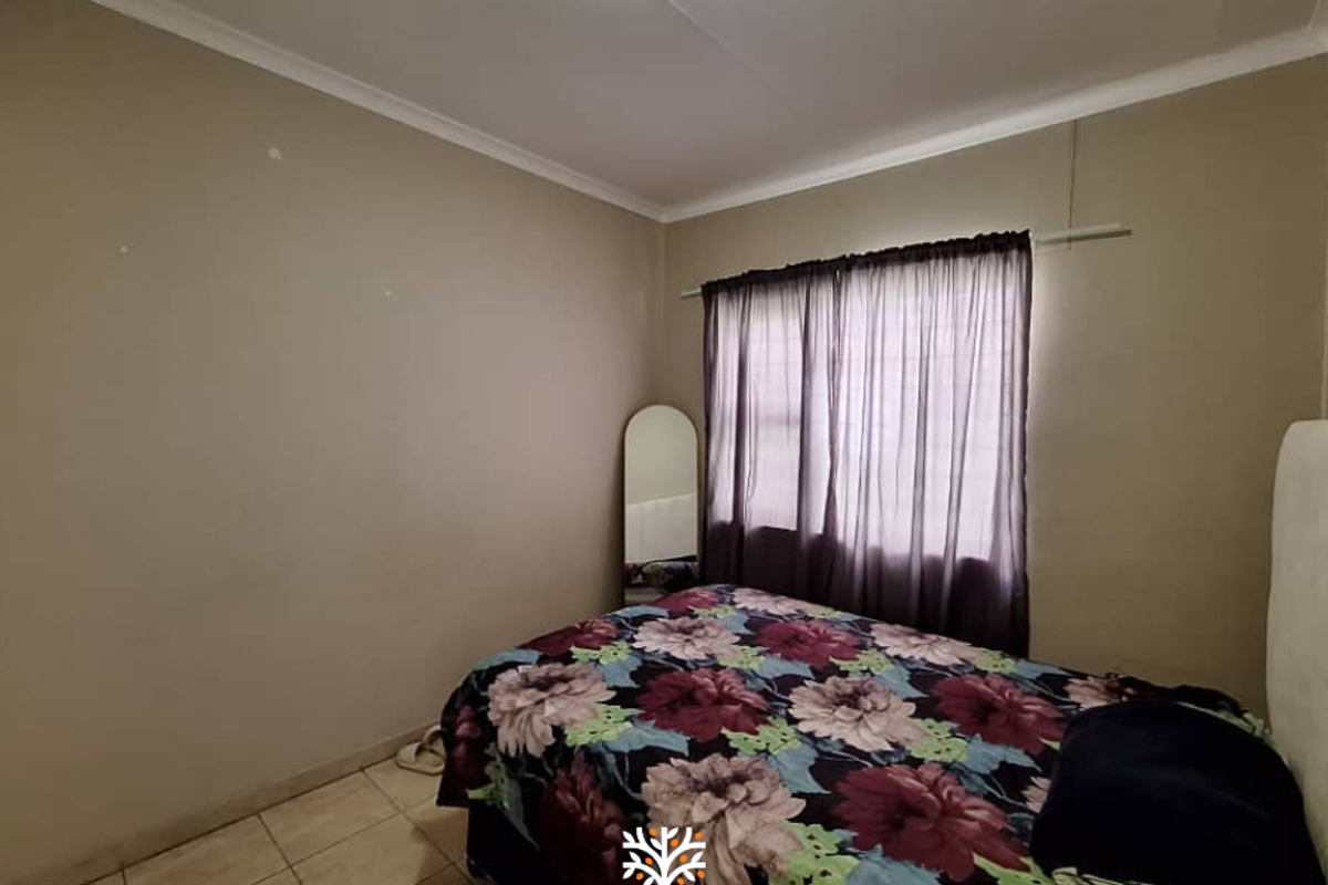 A functional bedroom featuring tiled flooring, neutral wall tones, and a window with fitted curtain rails.