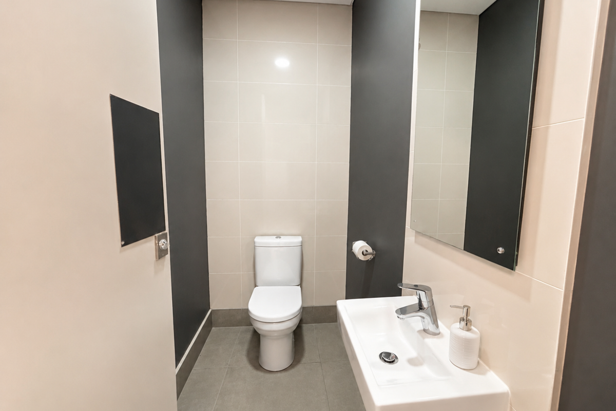 A modern, clean office restroom featuring a wall-mounted basin, a contemporary toilet, and a large wall mirror with neutral-toned tiled walls.